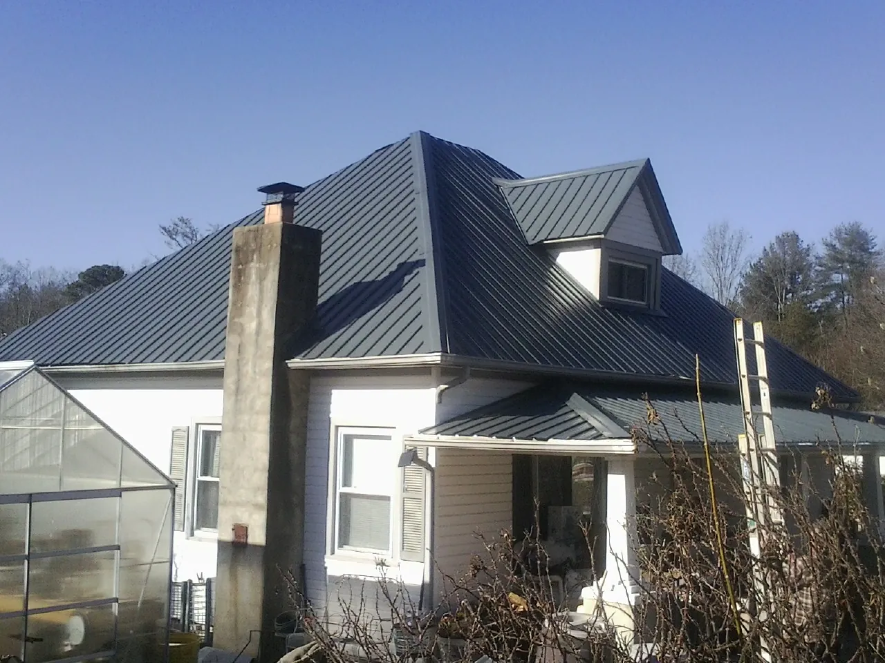 Dark blue standing seam metal roof on a white farmhouse with dormer — Slate & Tile Roof Repair by Roofing Brothers in Long Pine