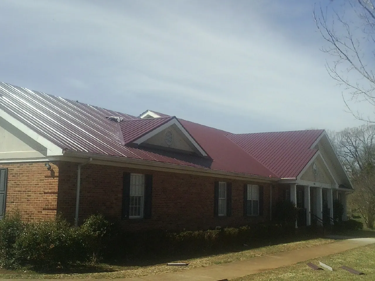Red metal roof with gabled entries on a long brick building, from a Hail Damage Roof Repair job in Long Pine