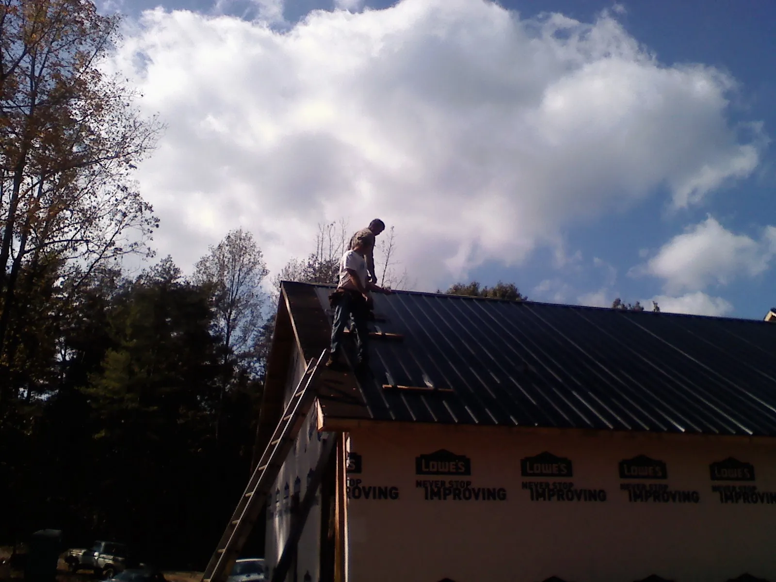 Roofer fastening dark metal panels high against a cloudy sky, from a Roof Inspection job in Long Pine